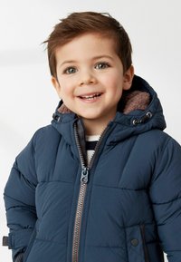 Marineblaue Steppjacke mit Reißverschluss vorne und braunem, gefüttertem Kapuzenkragen. Verfügt über ein gestepptes Design und Seitentaschen.