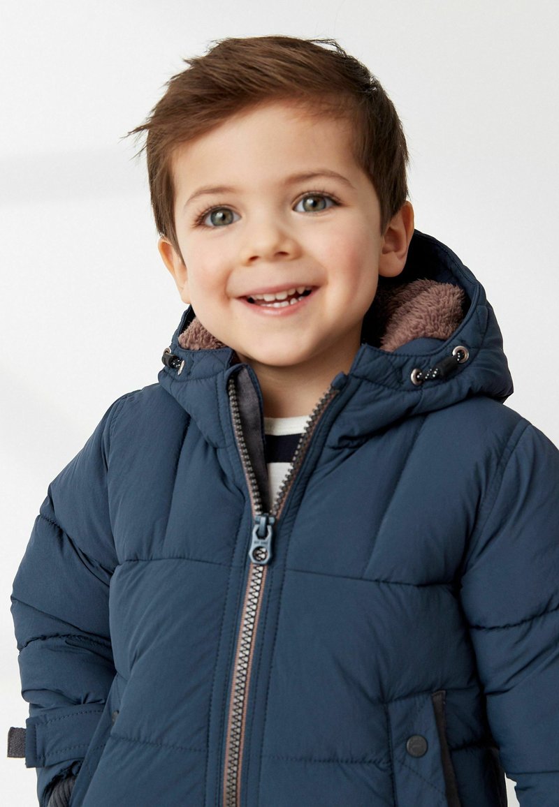 Marineblaue Steppjacke mit Reißverschluss vorne und braunem, gefüttertem Kapuzenkragen. Verfügt über ein gestepptes Design und Seitentaschen.