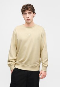 Μπεζ φούτερ με μακριά μανίκια και στρογγυλή λαιμόκοψη. Διαθέτει μικρό λευκό λογότυπο στο στήθος. Κατασκευασμένο από μαλακό, υφασμάτινο ύφασμα με υφή.