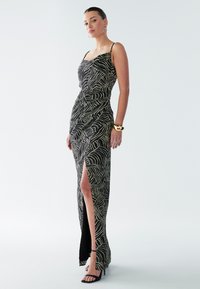 Black and gold patterned maxi dress with a fitted silhouette, thin straps, and a thigh-high slit. Smooth texture and elegant design details.