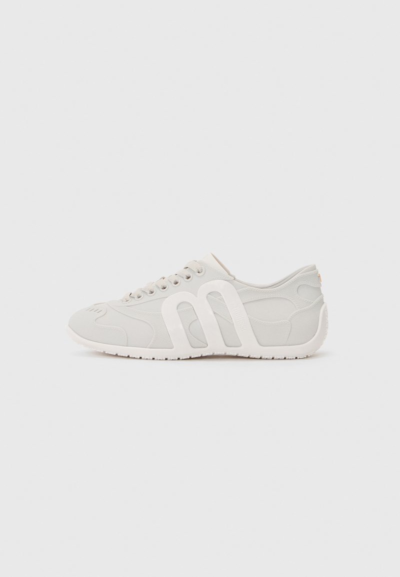 Light gray athletic shoe with smooth fabric and rubber sole, featuring a distinctive white logo, rounded toe, and minimalistic design.
