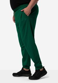 Groene joggers met zijzakken, elastische tailleband en verstelbaar trekkoord. Gecombineerd met zwarte sportschoenen met gestructureerde zolen.