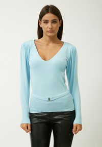 Maglione aderente azzurro chiaro con scollatura a V profonda, maniche lunghe, texture a costine e dettaglio in vita con cintura. Abbinato a pantaloni in pelle nera.