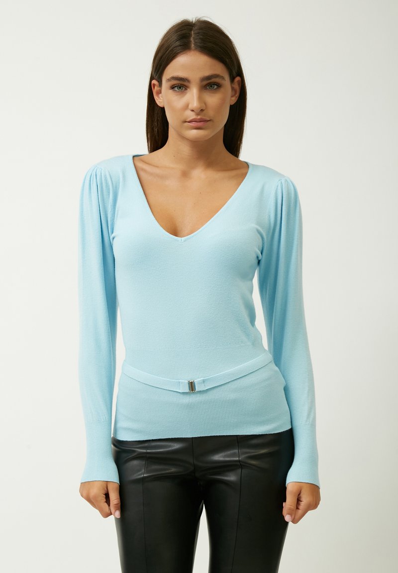 Maglione aderente azzurro chiaro con scollatura a V profonda, maniche lunghe, texture a costine e dettaglio in vita con cintura. Abbinato a pantaloni in pelle nera.