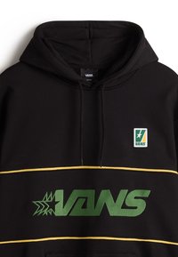 Svart huvtröja med känguruficka, grön "VANS"-logotyp, gula horisontella ränder och ett litet logopatch på bröstet. Mjuk tygkvalitet.