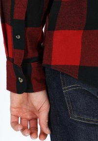 Rood en zwart geruit overhemd met lange mouwen en knoopmanchetten, gepresenteerd tegen donkere denim jeans. Het heeft een soepele textuur en een getailleerde pasvorm.
