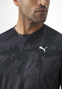 Schwarzes Sport-T-Shirt mit strukturiertem grafischen Muster und kleinem weißen Puma-Logo auf der Brust. Runder Ausschnitt, taillierte Passform.