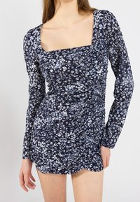 Marinblå blommig klänning med långa ärmar, fyrkantig halsringning och rynkad textur. Har små blålila och vita blommönster överallt.