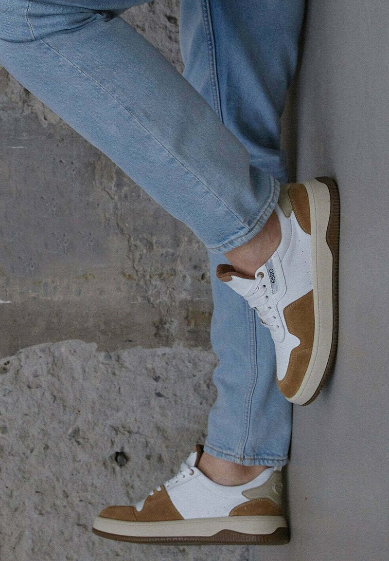 Bílé kožené tenisky s tanových semišovými akcenty, plochými šněrovadly a texturovanou hnědou gumovou podrážkou, umístěné na neutrálním pozadí.