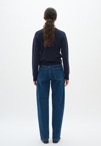 Marinblå tröja, blå hög midja jeans med raka ben, fem fickor och blå sömnadsdetaljer, bärs med svarta skor.