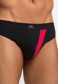 Brief in cotone nero con una striscia diagonale rossa, caratterizzato da un'etichetta logo sulla vita, progettato per una vestibilità aderente e flessibile.