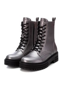 Botas de tobillo metálicas plateadas con cordones en la parte delantera, cuello acolchado y suela de goma negra gruesa. Cuenta con un zipper lateral para ponérselas fácilmente.