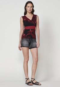 Top nero senza maniche con motivo floreale rosso e vita texturizzata, abbinato a pantaloni shorts in denim scuro sfilacciati e sandali neri con cinturini.