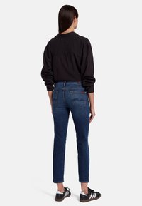 Tmavá košile s dlouhým rukávem, modré džíny s vysokým pasem, slim-fit design, rovné nohavice, jemné whiskering a dvě zadní kapsy, v kombinaci s černými teniskami.