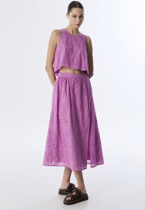 Top senza maniche rosa con motivo ricamato e una gonna abbinata. L'outfit presenta una vestibilità comoda e una silhouette fluida. Sandali marroni con borchie.