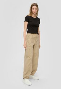 Zwart geribbelde top met korte mouwen gecombineerd met beige cargopantalons met zijzakken en elastische boorden, aangevuld met witte sneakers.