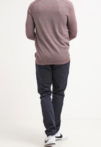 Bordeaux gebreide trui met een gestructureerde afwerking, gecombineerd met donkere marineblauwe broek. Witte sneakers met zwarte accenten maken de outfit compleet.