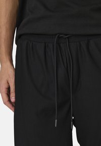 Joggers negros acanalados con cinturilla elástica ajustable, que cuentan con bolsillos laterales y un corte relajado. La tela texturizada aporta interés visual.