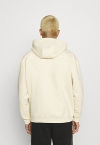 Krémová mikina s velkou kapucí, žebrovanými manžetami a lemem. Měkká, hladká textura. Jednoduchý, neformální design bez viditelných vzorů.