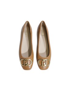 Ballerine in pelle color cuoio con punta rotonda, caratterizzate da una grande fibbia a logo dorato sul davanti e una finitura liscia e lucida.