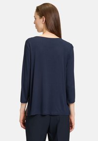 Mörkblå topp med trekvartsärmar och rund halsringning. Tillverkad av ett smidigt, lätt tyg med en avslappnad passform och enkel design.