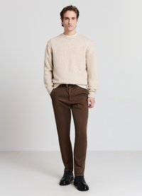 Beiger Strickpullover mit Sprenkeln, braune Hose und schwarze Lederstiefel. Das Outfit ist lässig und figurbetont, mit schlichtem Design.