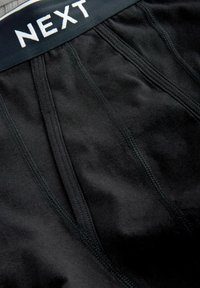 Boxers pour hommes noirs avec des coutures visibles et une ceinture étiquetée "NEXT" en lettres blanches.
