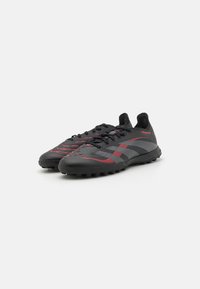 Scarpe nere con materiale testurizzato, dotate di accenti e strisce rosse. Suola in gomma con battistrada per trazione, progettate per l'uso sportivo.