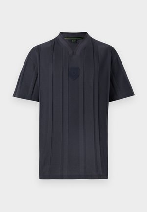 Chemise à manches courtes gris foncé avec des rayures verticales, un col en V fendu et un petit emblème en forme de bouclier sous l'encolure.