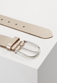 Ceinture en cuir texturé beige avec une boucle à double ardillon en argent et cinq trous de réglage, présentant un bord lisse et un design classique.