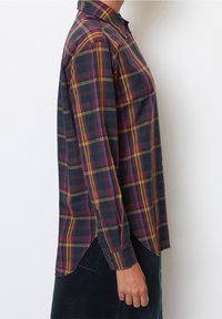 Camicia a maniche lunghe a quadri con quadrati blu scuro, gialli e viola, colletto con bottoni e spacchi laterali per facilitare il movimento.