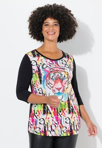 Kleurrijke T-shirt met een tijgerafbeelding op een achtergrond met een multikleurig letterpatroon. Zwarte driekwartmouwen, ronde halslijn, zachte stof.