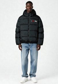 Doudoune noire à capuche, avec le message brodé "I ❤️ YOU" en rouge et blanc. Portée avec un jean bleu clair et des baskets blanches.