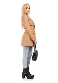 Beige op maat gemaakte blazer, dubbelgebreid, gestructureerde pasvorm. Lichtblauwe skinny jeans, zwarte platform enkellaarsjes en een kleine zwarte handtas.