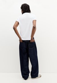 Tricou alb cu mâneci scurte asortat cu blugi lejeri, de culoare albastru închis. Blugii au un design clasic cu cinci buzunare și cusături în contrast.
