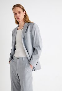 Completo grigio chiaro realizzato in tessuto testurizzato, con giacca sartoriale dotata di una tasca singola, abbinato a un top beige aderente.