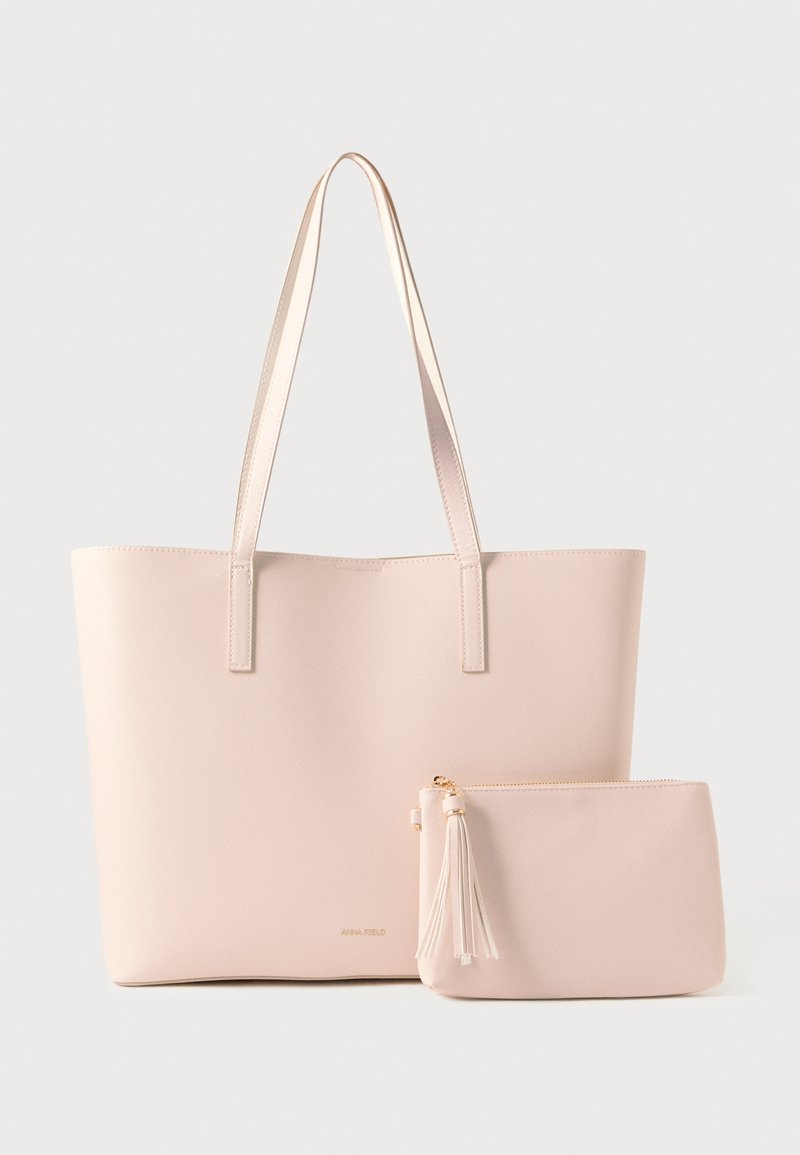 Grand sac cabas rose clair avec deux anses et une petite pochette assortie munie d'une fermeture éclair à pompon, le tout posé sur un fond blanc.
