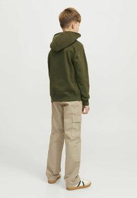 Grön huvtröja med avslappnad passform, i kombination med beiga cargobyxor med sidofickor och rak skärning. Sneakers med gröna accenter.