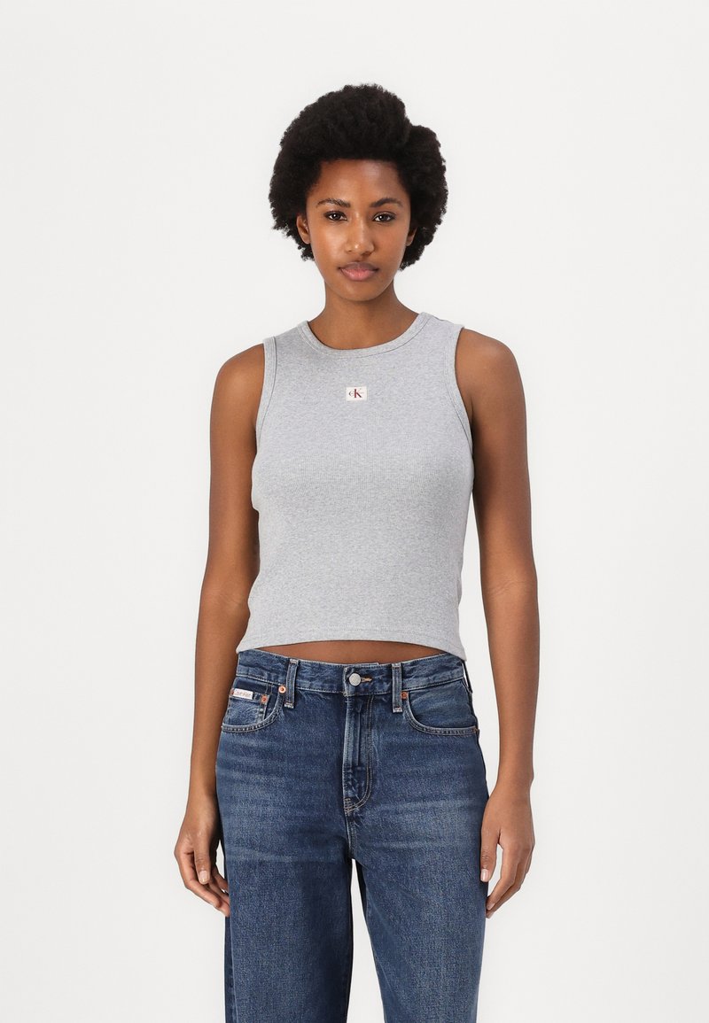 Grijze geribbelde tanktop met een ronde halslijn en een klein merklabel, gecombineerd met hoge blauwe spijkerbroek met typische stiksels.