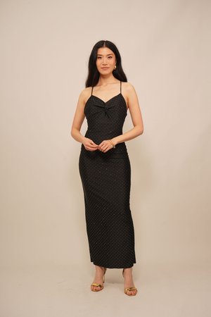 Black midi dress with white polka dots, spaghetti straps, a knotted detail at the bust, and a fitted silhouette. Worn with gold sandals.