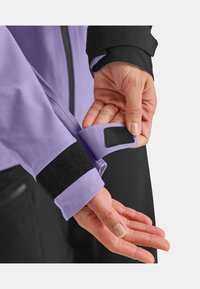 Light purple jacket sleeve with black cuff; features a Velcro strap for adjustment. Smooth texture, waterproof material, and contrasting colors.