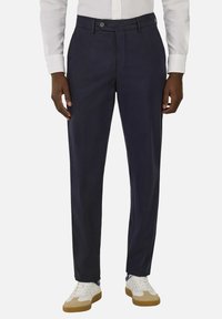 Navy trousers made of lightweight fabric, featuring a tailored fit, front pockets, and a button closure, paired with white sneakers.