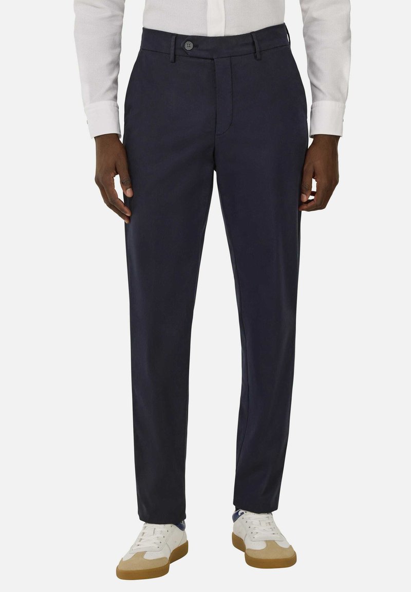 Navy trousers made of lightweight fabric, featuring a tailored fit, front pockets, and a button closure, paired with white sneakers.
