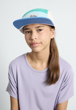 Baseballmütze mit mehrfarbigen Paneelen (türkis, weiß, blau) und einem Stoffaufnäher; kombiniert mit einem hellen lila T-Shirt. Glatte Texturen sichtbar.