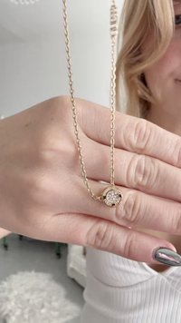 Zelta kaklarota ar apaļu kulonu, kura centrā ir kristāls, attēlota uz rokas, izceļot plānu ķēdi un pulētu apdari.