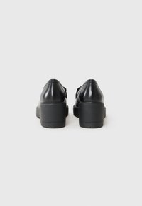 Chaussures à plateforme en cuir noir avec un bout rond, texture lisse et un talon épais ; design simple sans matériel ou motifs visibles.