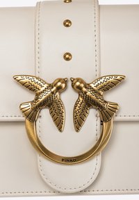 Borsa in pelle bianca con una chiusura in metallo dorato a forma di due uccelli, con incisioni dettagliate e borchie decorative sulla patta.