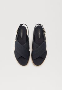 Sandalias de talón con correa en azul marino, diseño de tiras cruzadas, tejido texturizado, plantilla acolchada y suela de goma marrón. Detalle de acento en hardware dorado.