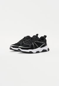 Fekete hálós és velúr sneaker fehér díszítéssel, vastag talppal, fűzőrendszerrel és logóval az oldalon. Tartós és sportos dizájn.