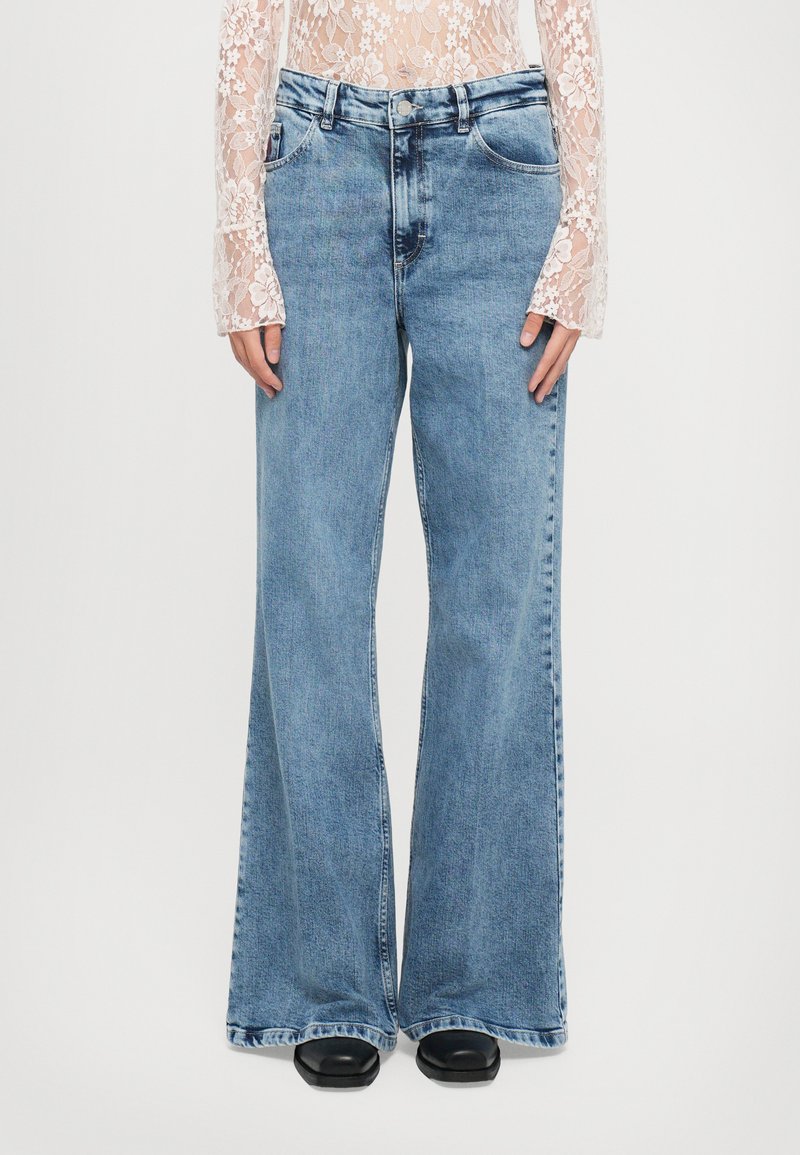 Jeans de mezclilla de tiro medio, en azul claro, con corte acampanado, diseño de cinco bolsillos y detalle deshecho en los puños. Presentan una textura desteñida.